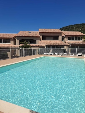 Una piscina rettangolare con acqua cristallina e azzurra, circondata da una recinzione bianca.