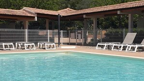 A swimming pool with sun loungers and a covered area, surrounded by a fence and greenery in the background. - 3 bedroom apartment with swimming pool 3km from St Florent  (Oletta)