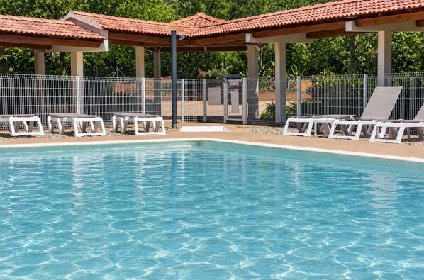 Ein Schwimmbecken mit klarem Wasser, umgeben von weißen Liegestühlen und einem überdachten Bereich mit Flachdach.