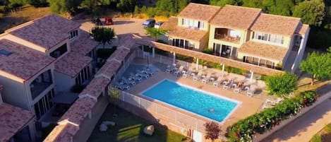 A residential area with a swimming pool surrounded by lounge chairs and a covered patio.