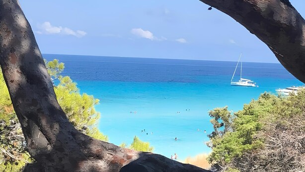 A beach with clear turquoise water, a sailboat, and a rocky landscape with trees. - 3 bedroom apartment with swimming pool 3km from St Florent  (Oletta)