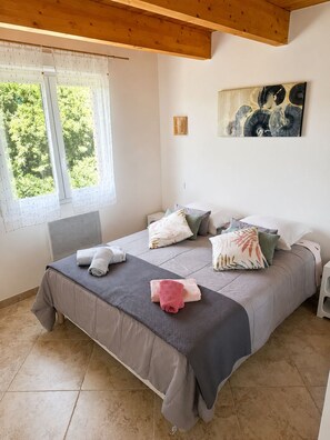 Ein Schlafzimmer mit einem Bett, Kissen, einem Fenster und einem Bild an der Wand.
