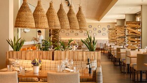 Un restaurante con barra de madera, varias mesas y lámparas colgantes de fibras.