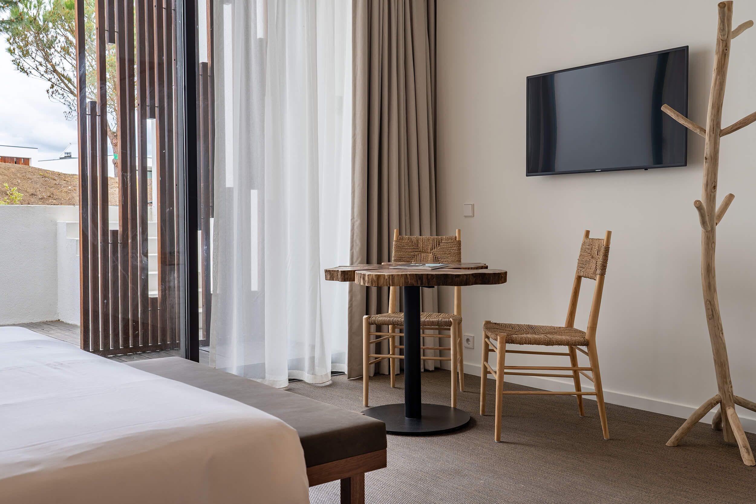 A hotel room with a bed, a small round table with chairs, a television mounted on the wall, and a wooden chair.