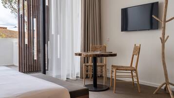 A hotel room with a bed, a small round table with chairs, a television mounted on the wall, and a wooden chair.