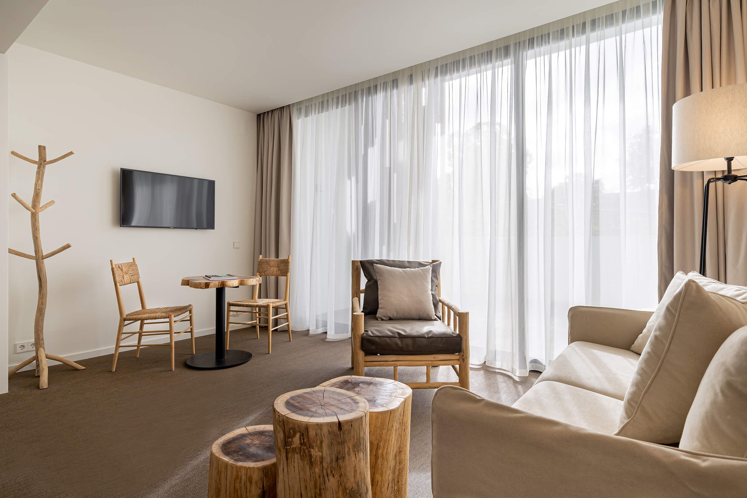 A modern living room with a sofa, a wooden chair, a round table, and a TV mounted on the wall.