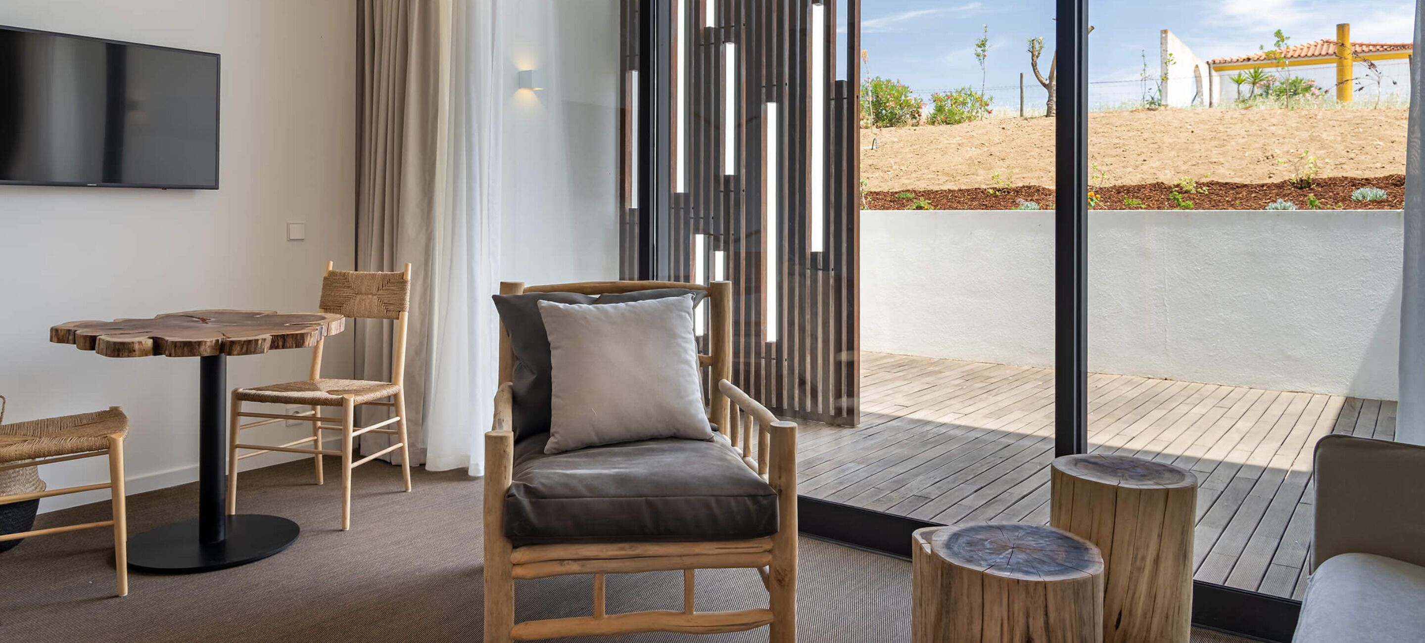 Een moderne kamer met een houten stoel, een klein rond tafeltje en uitzicht op een aangelegde tuin.