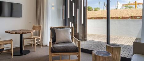 Een moderne kamer met een houten stoel, een klein rond tafeltje en uitzicht op een aangelegde tuin.