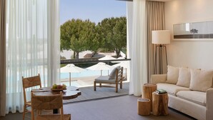 Habitación de hotel con balcón, sofá, mesa de comedor y sillas, y una lámpara.