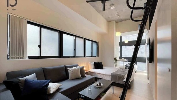 A modern hotel room with a sofa, a bed, a small table, and a ladder.