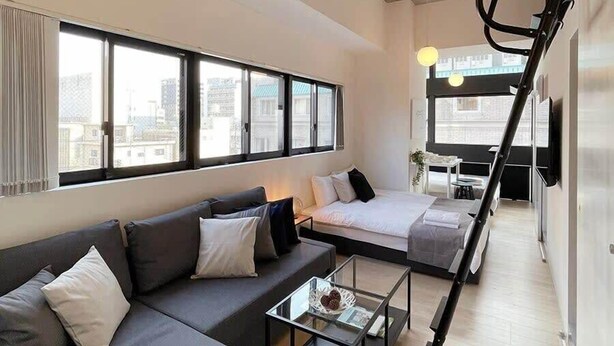 A modern hotel room with a sofa, a bed, a small table, and a staircase.