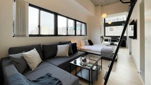 A modern hotel room with a sofa, a bed, a coffee table, and a view of the city through large windows.