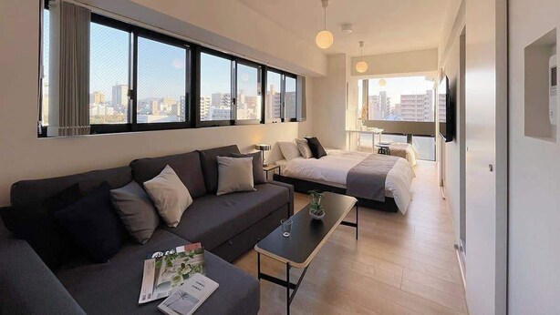 A modern hotel room with a sofa, a bed, a small table, and a TV. - b hotel Neko Yard | Modern City-Center Studio (Naka Ward, Hiroshima)