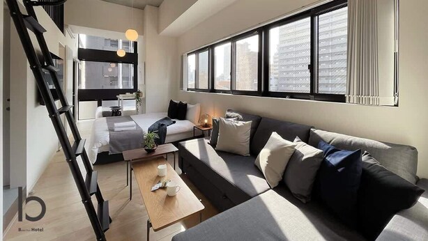 Ein modernes Hotelzimmer mit einer Couch, einem Couchtisch, einer Leiter und einem großen Fenster mit Jalousien.