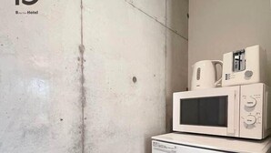 Una kitchenette compacta con microondas y un refrigerador pequeño, una cafetera y un tostador encima del microondas.