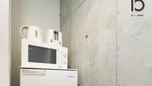 A compact, white Hisense refrigerator with a microwave on top, situated in a corner against a plain concrete wall.