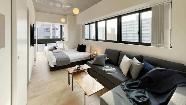 A modern hotel room with a bed, sofa, and a dining area.