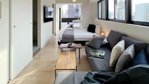 A modern hotel room with a minimalist design, featuring a sofa set, a coffee table, and a TV mounted on the wall. - b hotel Neko Yard | Sleek & Bright Urban Studio (Naka Ward, Hiroshima)