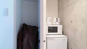 A compact kitchenette with a microwave and a small refrigerator, a brown towel hanging on the door, and a shelf above the refrigerator.