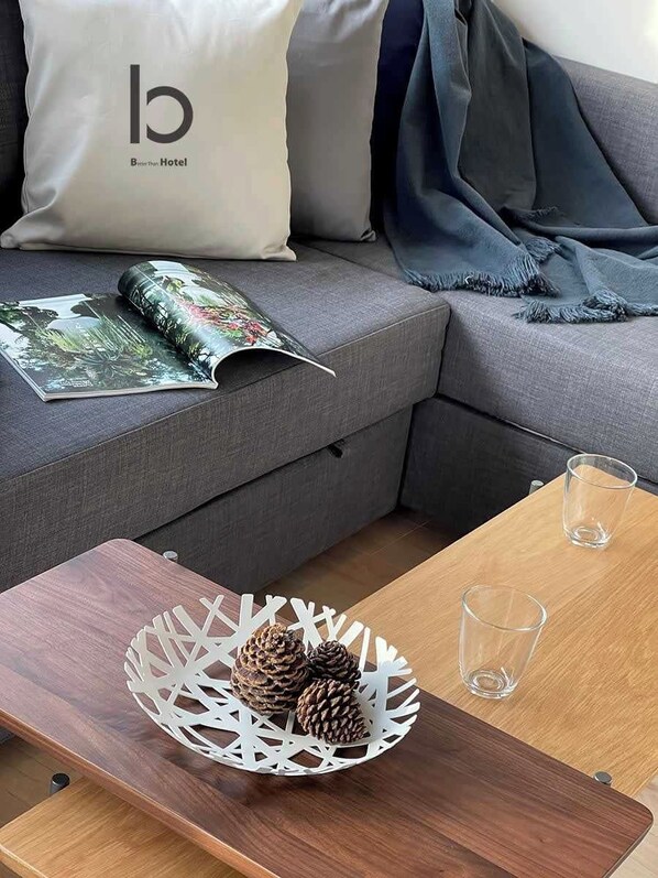A modern living room with a grey sofa, a magazine, a wooden coffee table with a pinecone decoration, and a glass on the table.