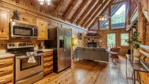 A log cabin interior with a kitchen, dining area, and a fireplace. - Dreamy Forest Home, 2 Decks, Hot Tub, Outdoor Pool | 10 Mins to Broadway, Perfect for Groups, 24 Hour Hospitality, Sleep 10 w/ Wraparound Deck, Scenic Views & Access to Resort Pool,  Near The Parkway, Tanger Outlets & Dollywood (Pigeon Forge)