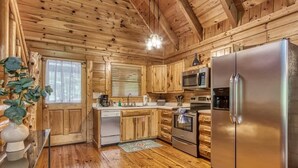 A wooden cabin interior with a kitchen featuring a stainless steel refrigerator, microwave, and oven. - Dreamy Forest Home, 2 Decks, Hot Tub, Outdoor Pool | 10 Mins to Broadway, Perfect for Groups, 24 Hour Hospitality, Sleep 10 w/ Wraparound Deck, Scenic Views & Access to Resort Pool,  Near The Parkway, Tanger Outlets & Dollywood (Pigeon Forge)