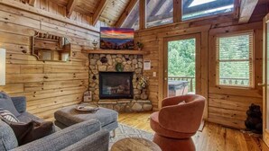 A cozy cabin interior with a stone fireplace, wooden walls, and a comfortable seating area. - Dreamy Forest Home, 2 Decks, Hot Tub, Outdoor Pool | 10 Mins to Broadway, Perfect for Groups, 24 Hour Hospitality, Sleep 10 w/ Wraparound Deck, Scenic Views & Access to Resort Pool,  Near The Parkway, Tanger Outlets & Dollywood (Pigeon Forge)