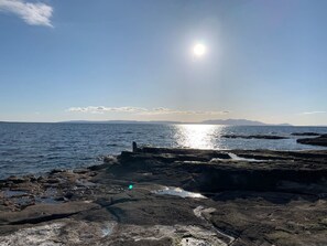 A rocky shoreline with calm water and distant mountains under a clear sky. - Troon Golf & Beach Haven (Troon)