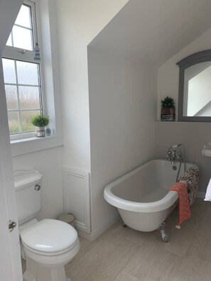 A bathroom with a toilet, a bathtub, and a window with a plant. - Troon Golf & Beach Haven (Troon)