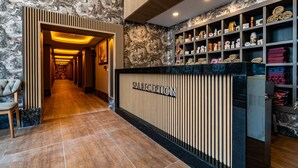 Zona de recepción con pared de mármol, mostrador de recepción y estanterías con diversos objetos.