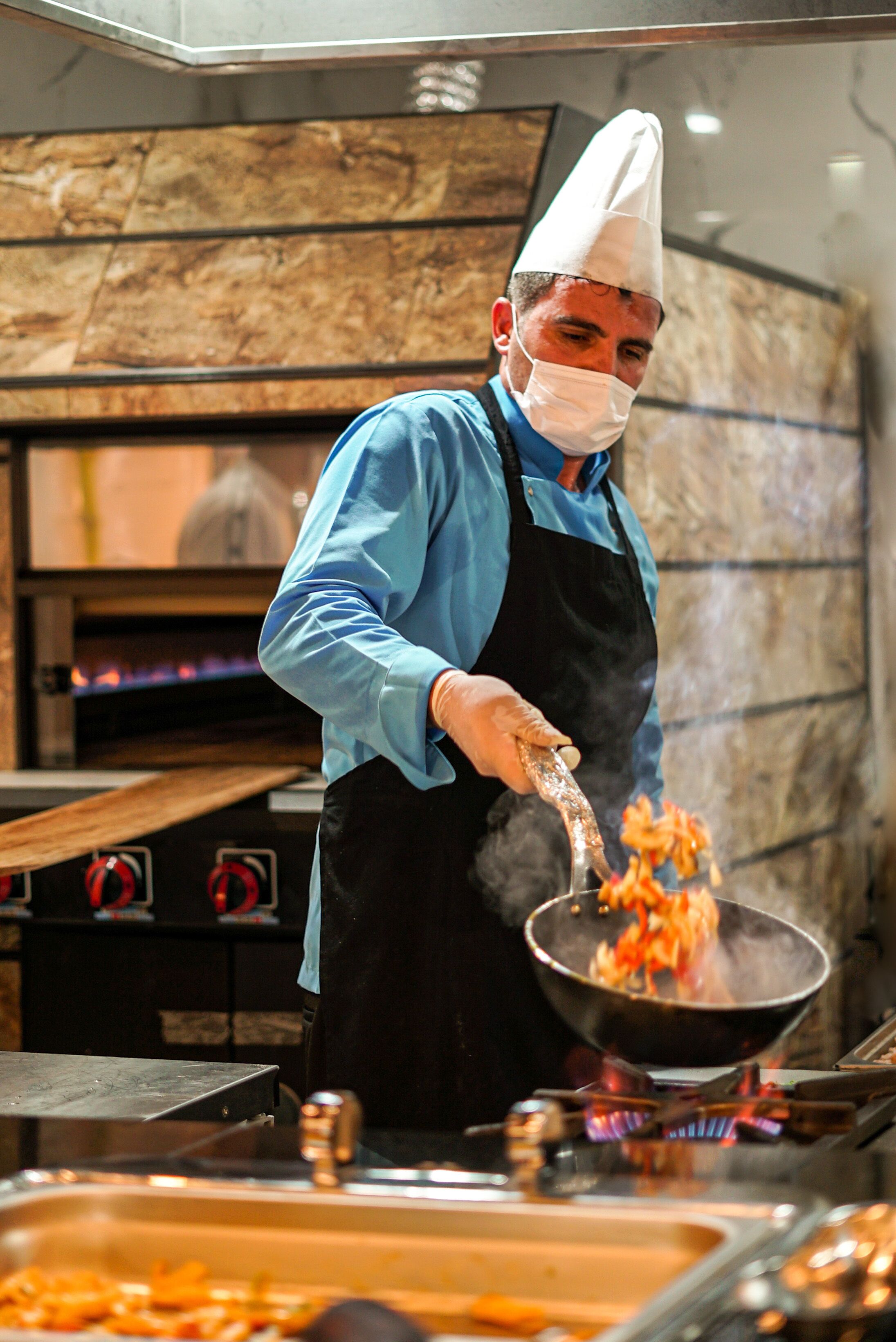 Um chef cozinha numa cozinha profissional com parede de pedra e forno a lenha.