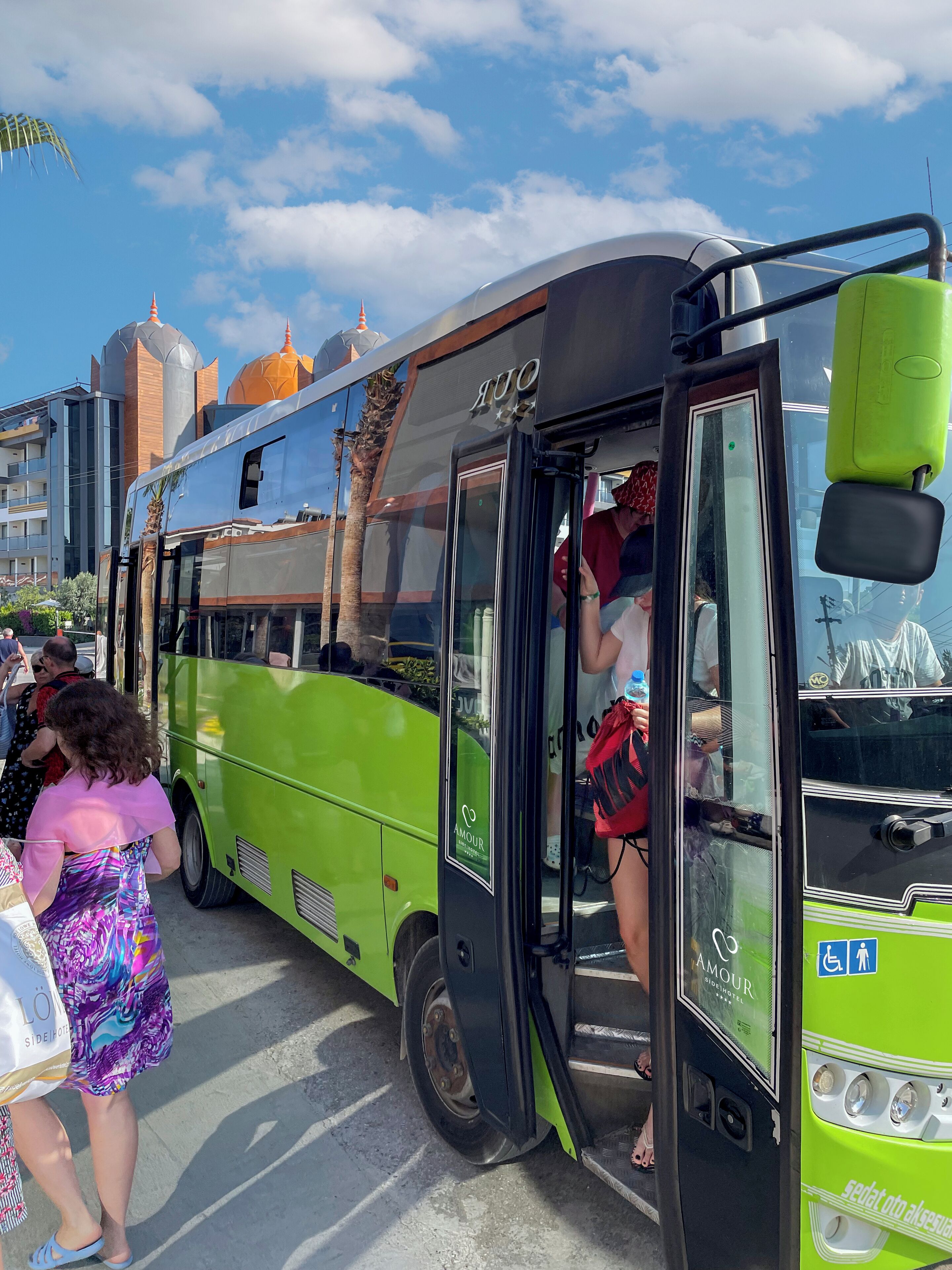 Ein grüner Bus mit Nebentür, geparkt in einer Stadt, im Hintergrund Gebäude und ein klarer Himmel.