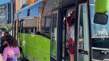 Ein grüner Bus mit Nebentür, geparkt in einer Stadt, im Hintergrund Gebäude und ein klarer Himmel.