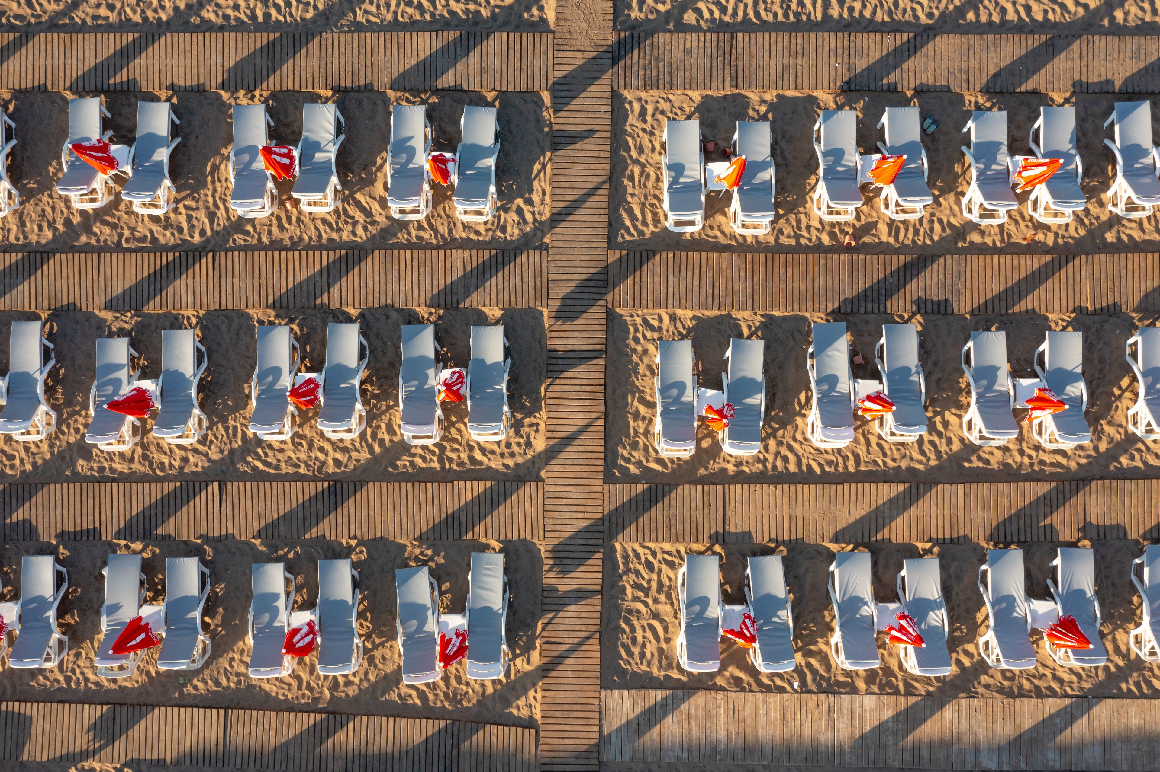 A beachside hotel with rows of sun loungers and umbrellas, arranged in a grid pattern on the sand and wooden deck.