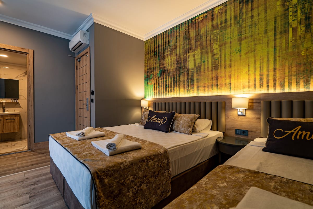 A hotel room with a large bed, a bedside table, a nightstand, a wall-mounted air conditioner, and a bathroom visible through an open door.