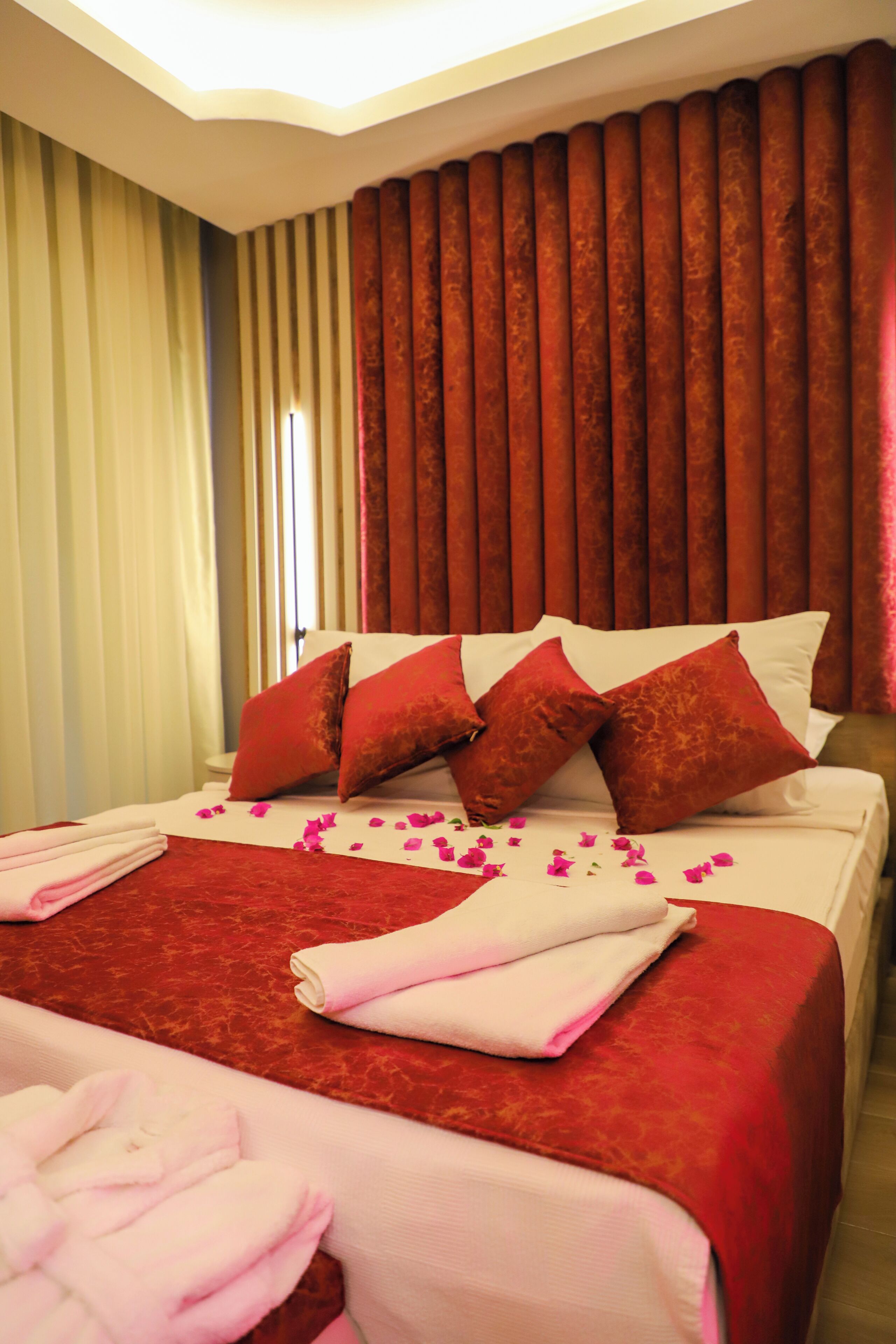 A hotel room with a large bed, red and white bedding, and a curtain backdrop.