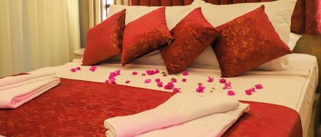 A hotel room with a large bed, red and white bedding, and a curtain backdrop.
