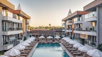 Un hotel moderno con piscina central rodeada de sillones de descanso y sombrillas, con varios pisos y balcones, además de una tienda de spa.