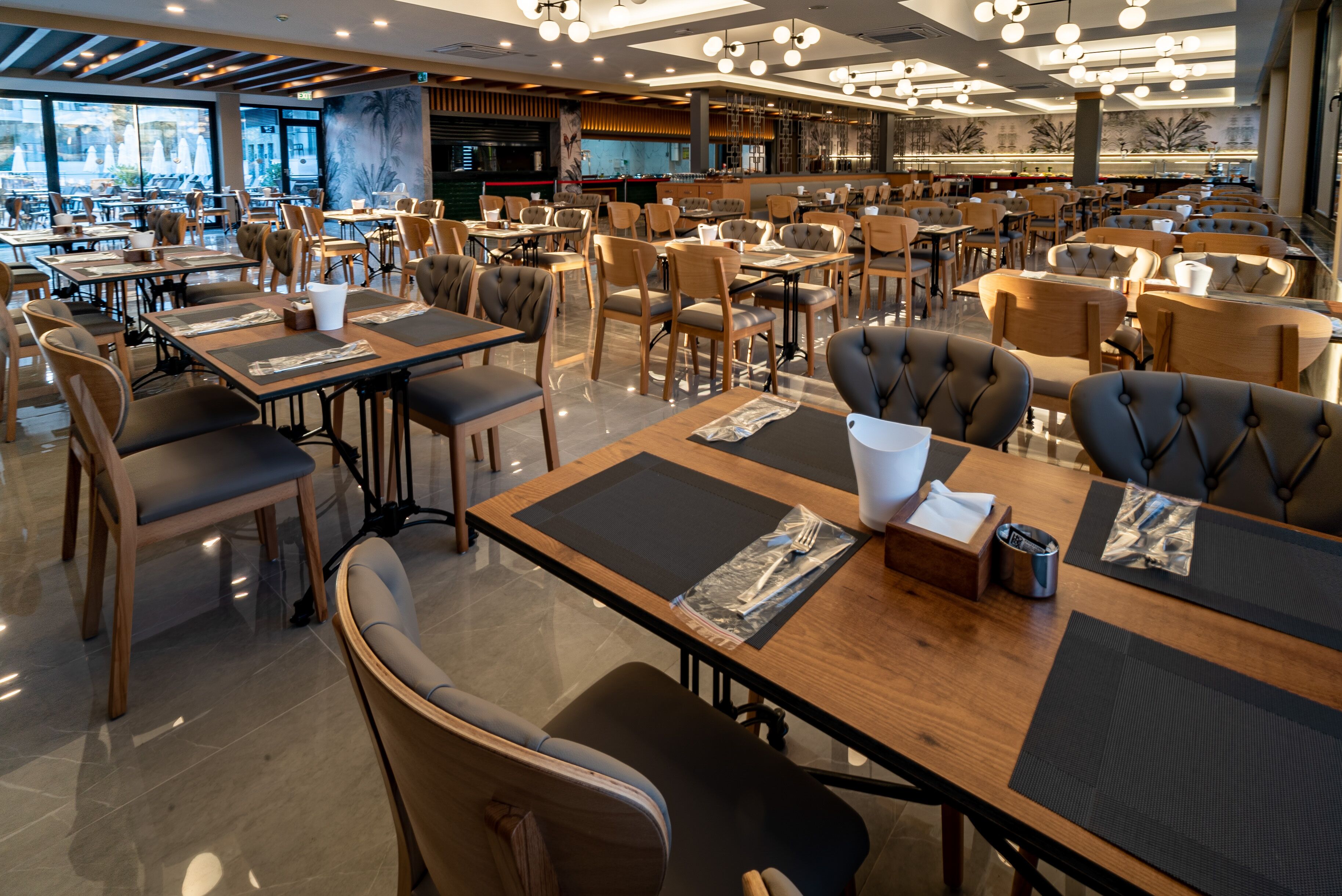 Un restaurante espacioso con varias mesas y sillas, una zona de bar y amplios ventanales con vistas a la calle.
