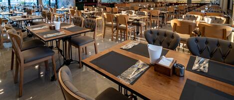 Un restaurante espacioso con varias mesas y sillas, una zona de bar y amplios ventanales con vistas a la calle.