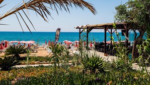 Un área frente a la playa con mesas al aire libre, sombrillas y una estructura de madera.