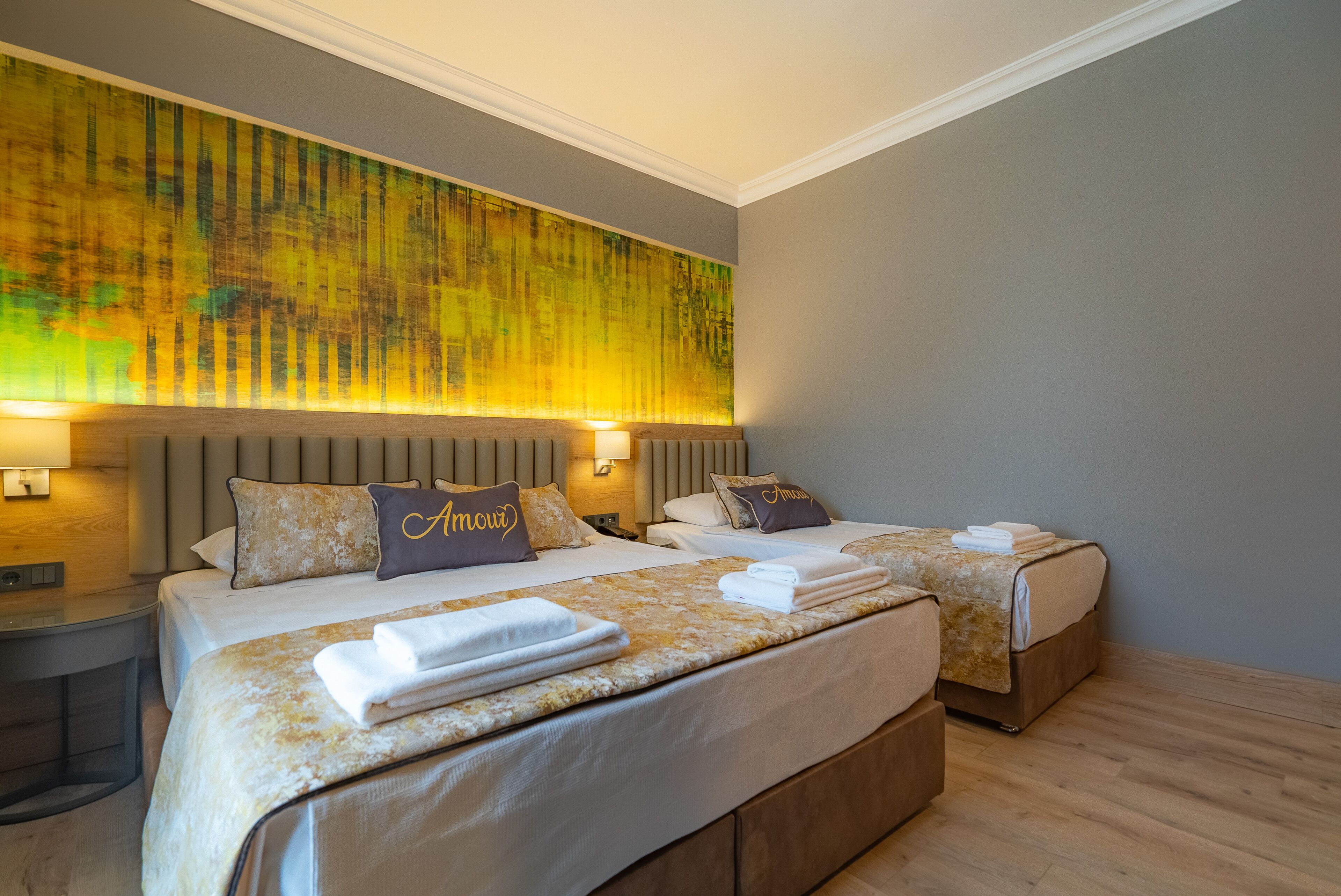 A hotel room with two beds, each with a headboard, a large abstract painting on the wall, and a wooden floor.