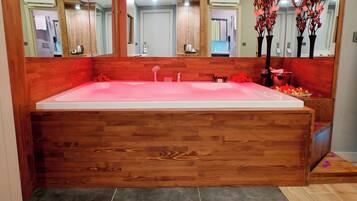 Una bañera de madera grande con un espejo arriba, un banco de madera pequeño y una bandeja con artículos de tocador.