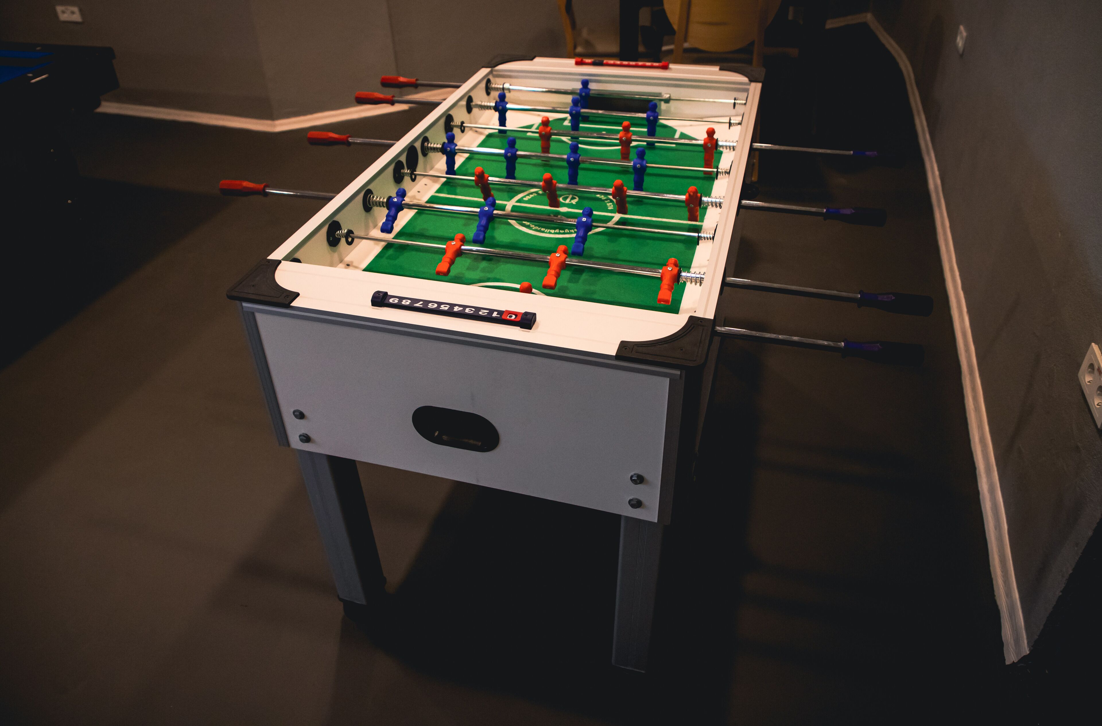 Uma mesa de futebol de mesa com superfície de jogo verde e figuras de jogadores vermelhas e azuis.