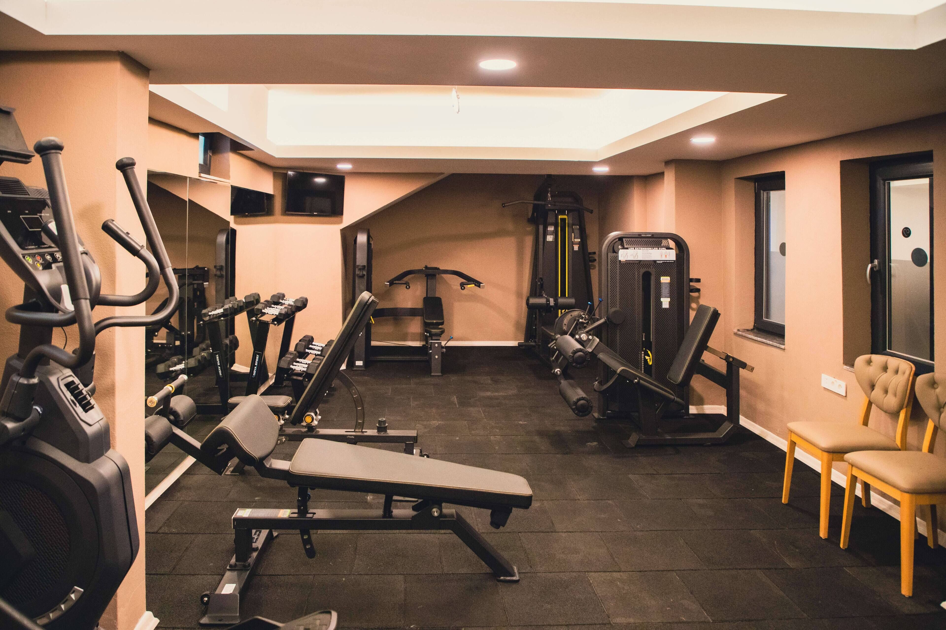 Een sportschool met diverse fitnessapparaten, waaronder loopbanden, krachttoestellen en een bank.