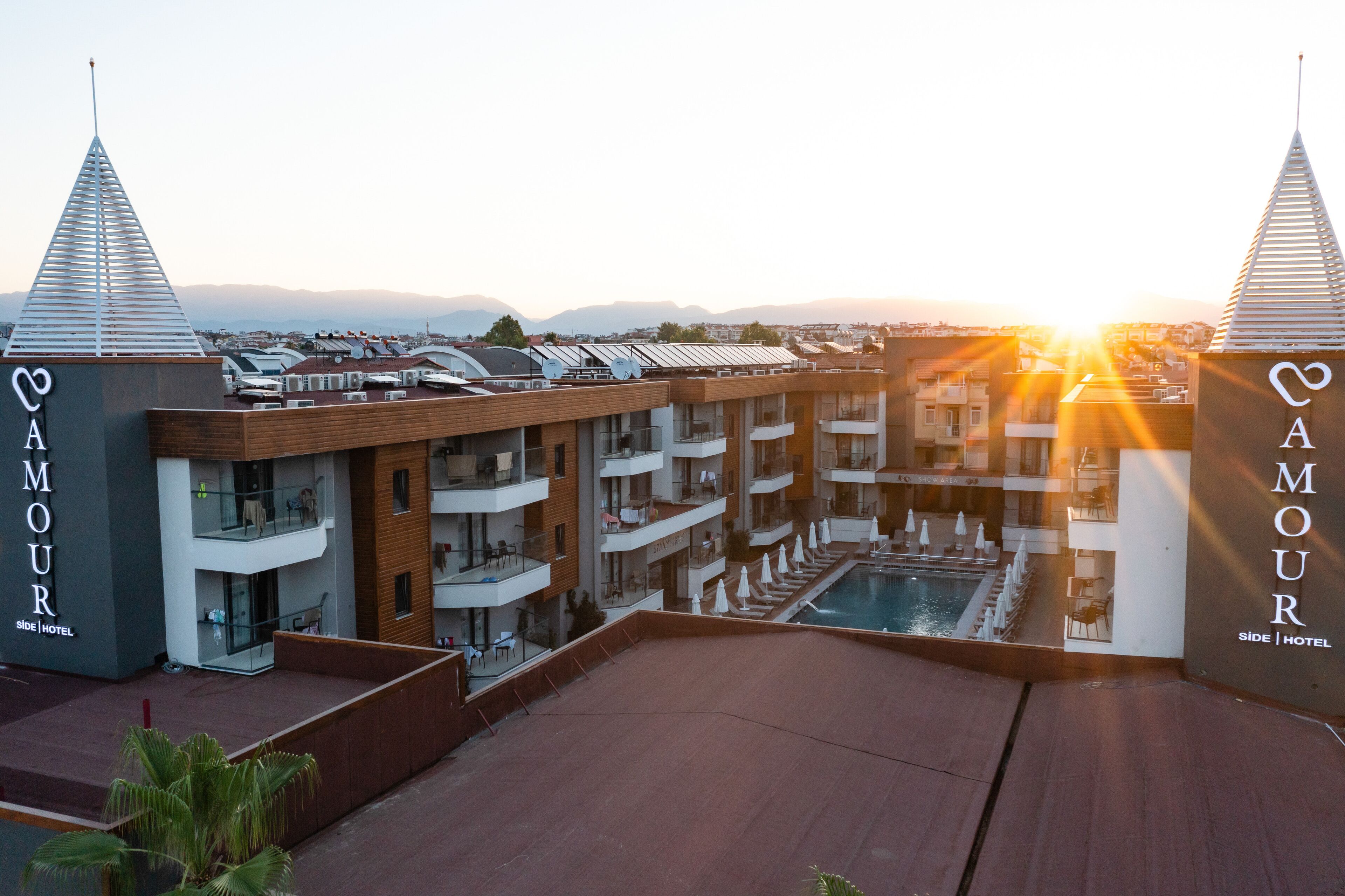 A hotel with a rooftop pool, multiple balconies, and a view of the sunset.