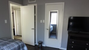 Une chambre avec deux lits, une télévision, une commode et une porte donnant sur une autre pièce.