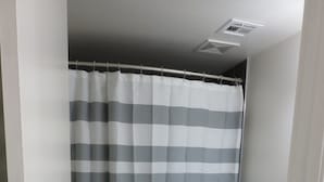 Une salle de bain avec un rideau de douche à rayures, des toilettes blanches et un lavabo avec un meuble sombre.