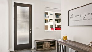 Una entrada moderna con una puerta oscura, un aparador de vidrio con naranjas y un cartel de bienvenida.