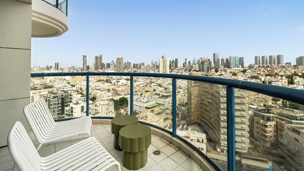 Un balcón con sillas blancas y una pequeña mesa, con vistas a un paisaje urbano con diversos edificios.